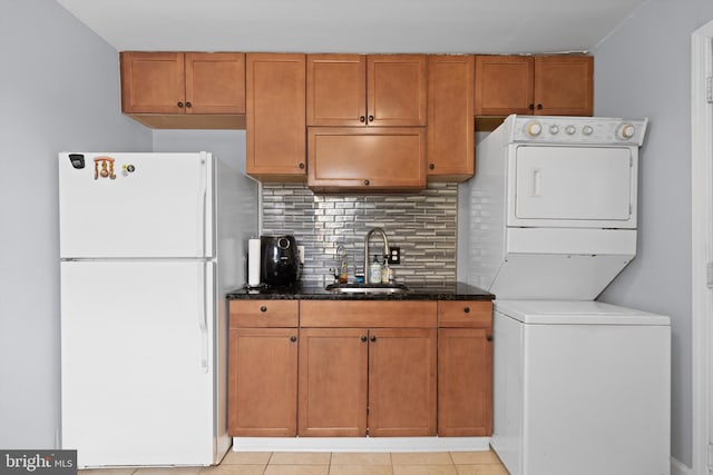 kitchen with sink, tasteful backsplash, white refrigerator, stacked washer / dryer, and light tile patterned flooring