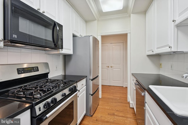 kitchen with appliances with stainless steel finishes, white cabinetry, sink, ornamental molding, and light wood-type flooring