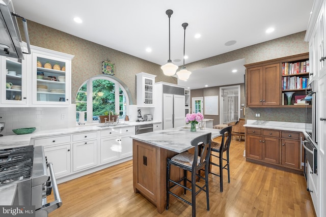 kitchen with white cabinetry, hanging light fixtures, backsplash, a center island, and light stone countertops