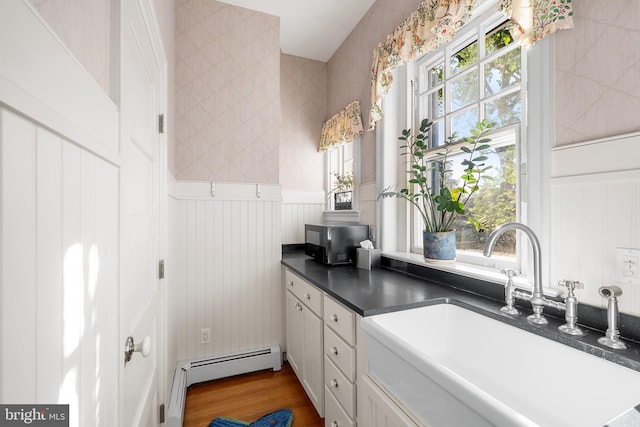 kitchen with white cabinetry, a baseboard radiator, wood-type flooring, and sink