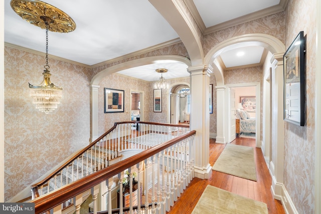 hall with ornate columns, a notable chandelier, ornamental molding, and light wood-type flooring