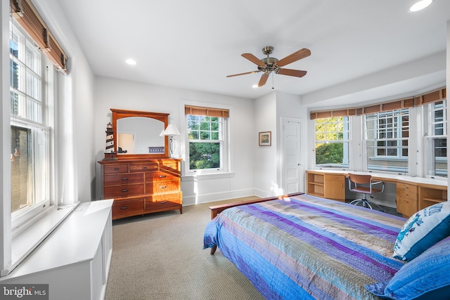 bedroom featuring built in desk, light colored carpet, and ceiling fan