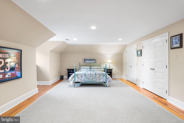 bedroom with lofted ceiling, light hardwood / wood-style floors, and two closets