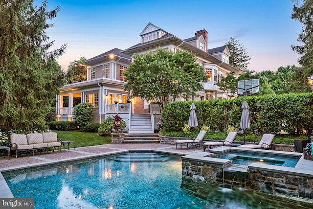 back house at dusk featuring a swimming pool with hot tub and a patio area