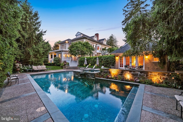 pool at dusk featuring an in ground hot tub and a patio area