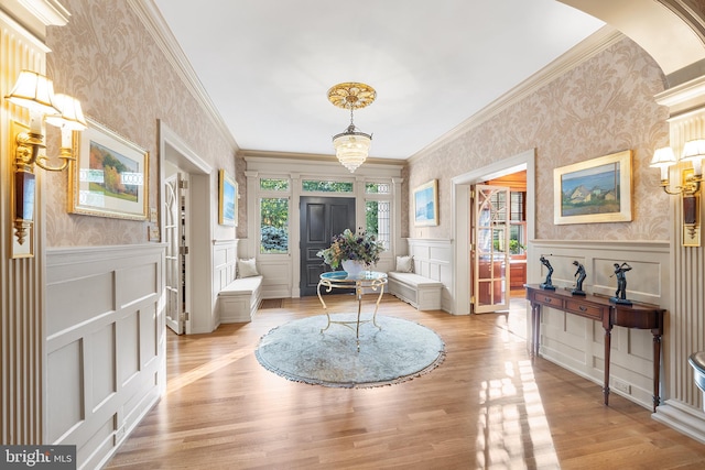 entryway with ornamental molding, a chandelier, and light wood-type flooring