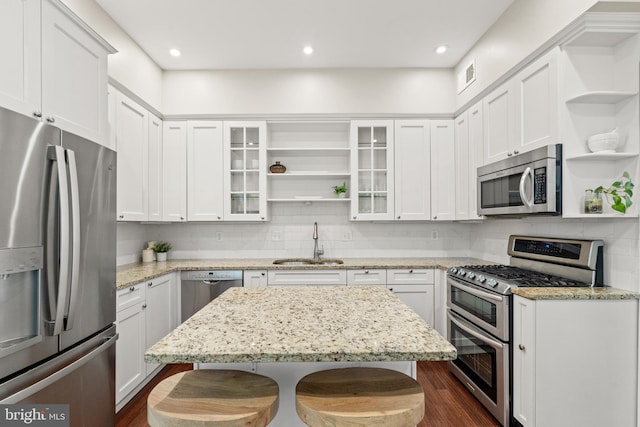 kitchen featuring white cabinets, sink, light stone countertops, appliances with stainless steel finishes, and a kitchen bar