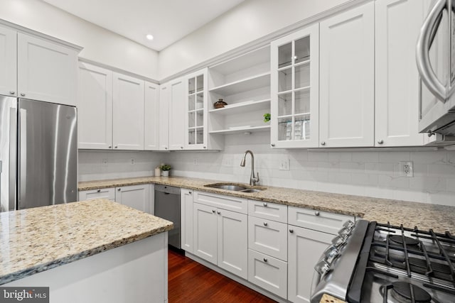 kitchen with light stone countertops, appliances with stainless steel finishes, tasteful backsplash, sink, and white cabinetry