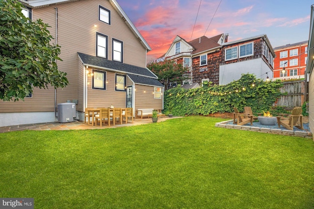 back house at dusk featuring a lawn and a patio area