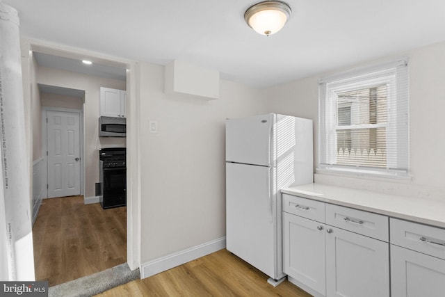 kitchen with white cabinets, stove, white fridge, and light wood-type flooring