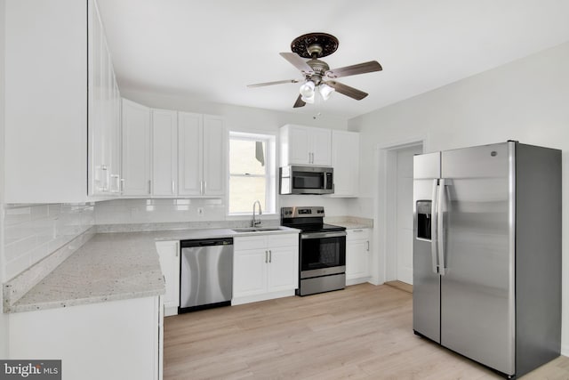 kitchen with light stone counters, stainless steel appliances, sink, light hardwood / wood-style floors, and white cabinetry