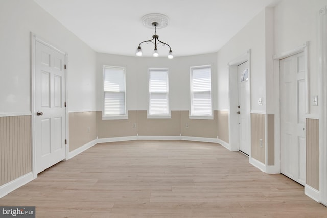 unfurnished dining area with an inviting chandelier and light wood-type flooring