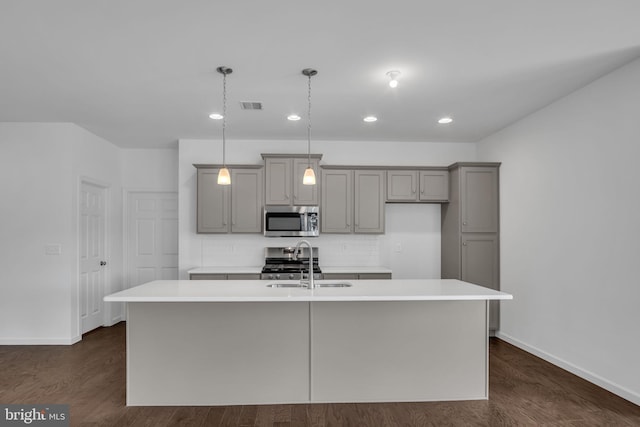 kitchen with pendant lighting, sink, stainless steel appliances, and a kitchen island with sink