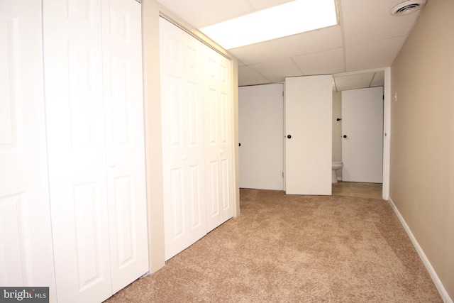 finished below grade area with visible vents, a paneled ceiling, light colored carpet, and baseboards