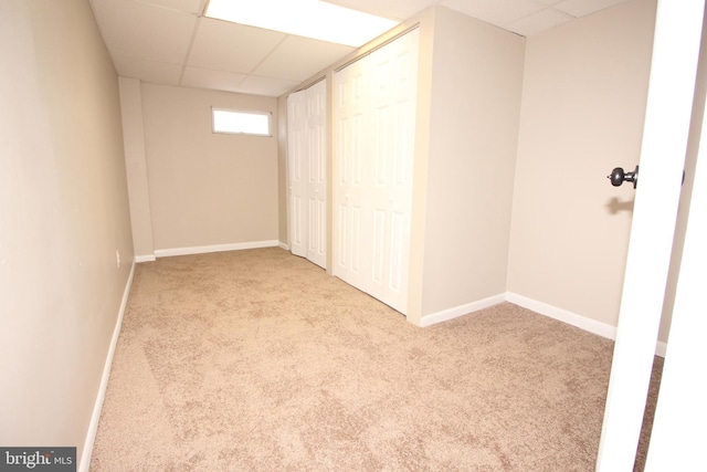 basement with carpet flooring, a paneled ceiling, and baseboards