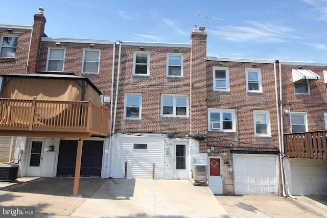 rear view of property with brick siding, central AC unit, an attached garage, and driveway