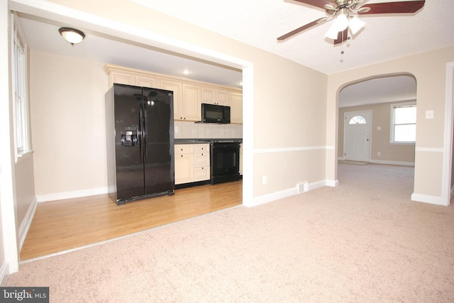 interior space featuring tasteful backsplash, light colored carpet, arched walkways, cream cabinetry, and black appliances