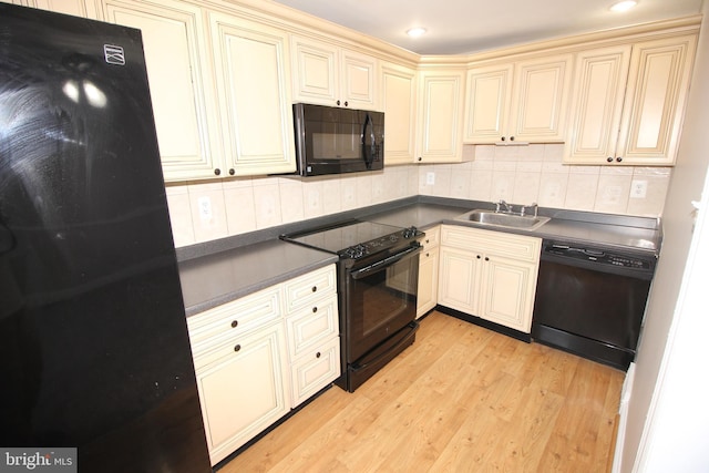 kitchen with black appliances, cream cabinetry, a sink, dark countertops, and light wood-style floors