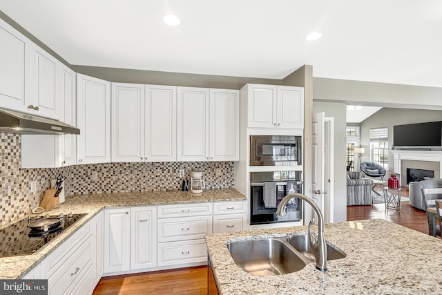 kitchen with black electric stovetop, white cabinets, stainless steel microwave, sink, and oven