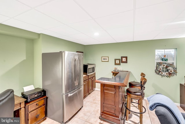 kitchen with kitchen peninsula, stainless steel appliances, light tile patterned floors, a paneled ceiling, and a breakfast bar area