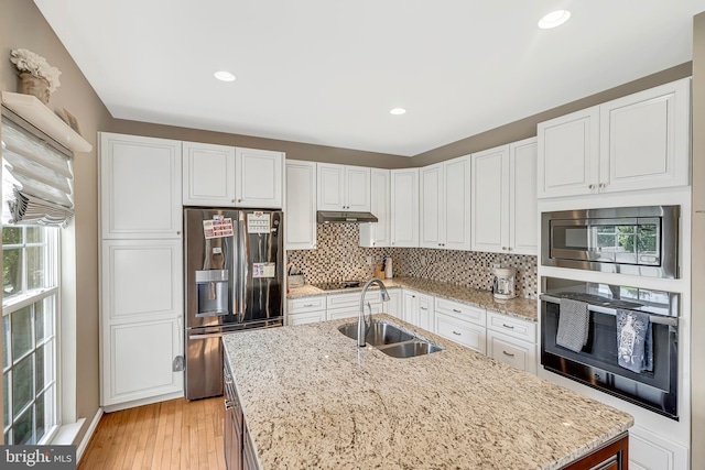 kitchen with a center island with sink, sink, light stone counters, appliances with stainless steel finishes, and white cabinets