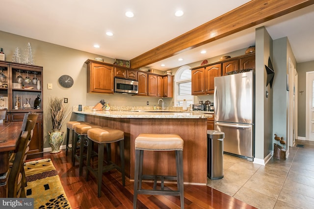 kitchen with a breakfast bar, sink, appliances with stainless steel finishes, beamed ceiling, and kitchen peninsula