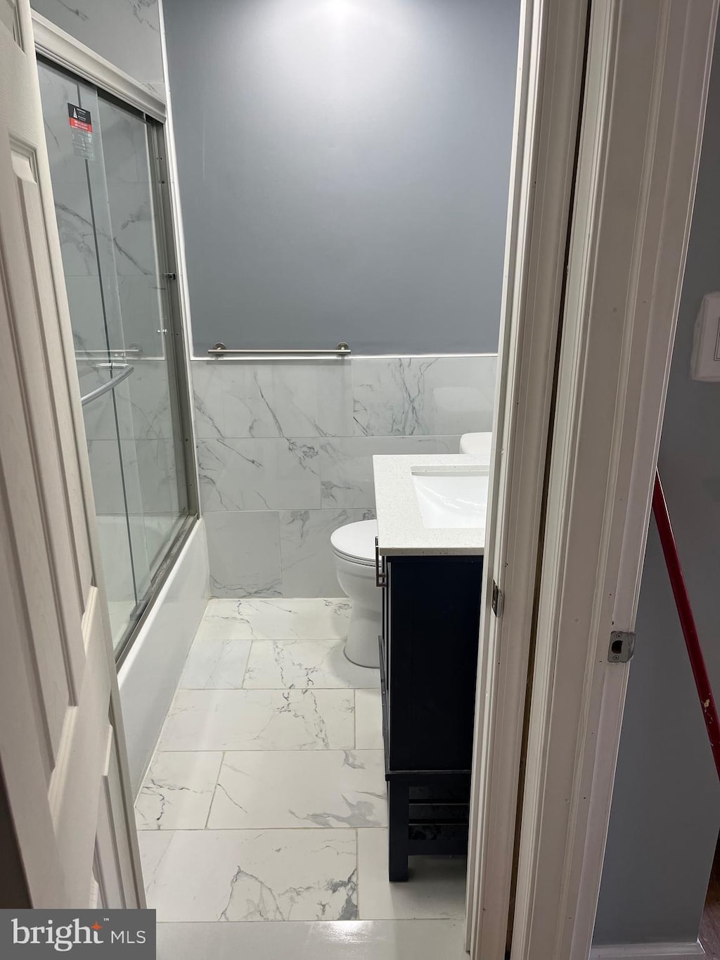 full bathroom with enclosed tub / shower combo, vanity, toilet, and tile walls