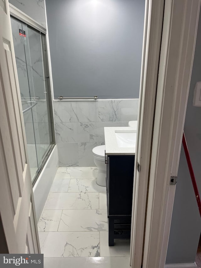 full bathroom featuring combined bath / shower with glass door, vanity, toilet, and tile walls