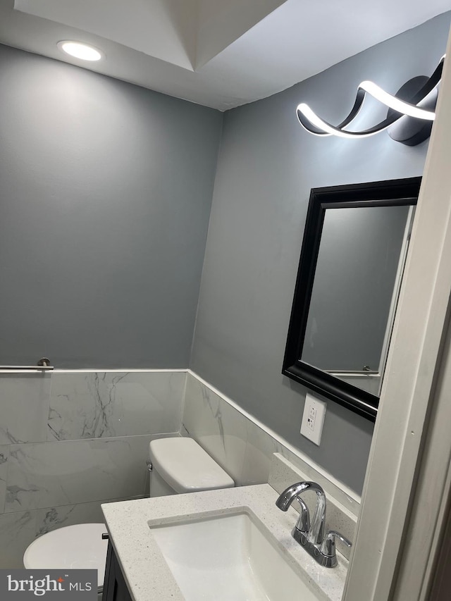 bathroom with vanity, tile walls, and toilet