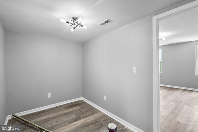 empty room featuring wood-type flooring and an inviting chandelier