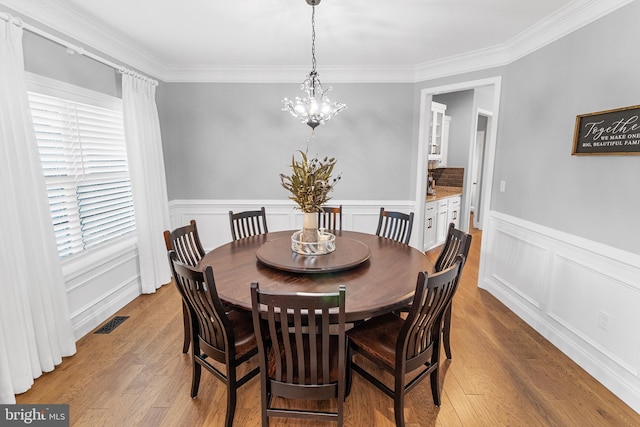 dining space with crown molding, light hardwood / wood-style floors, and an inviting chandelier