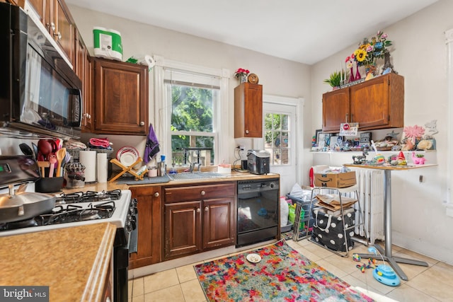 kitchen with radiator, sink, light tile patterned flooring, and black appliances