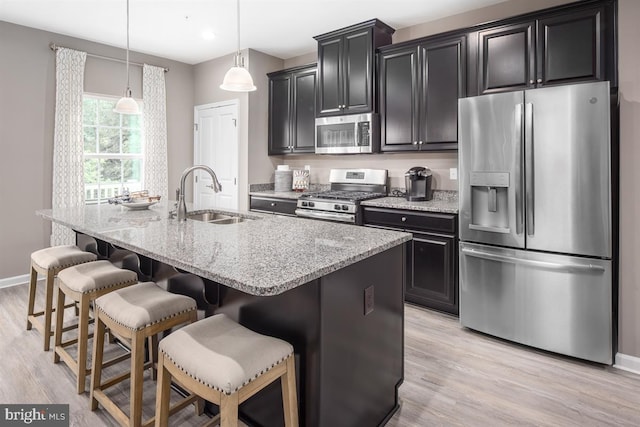 kitchen with appliances with stainless steel finishes, sink, a center island with sink, decorative light fixtures, and light hardwood / wood-style floors