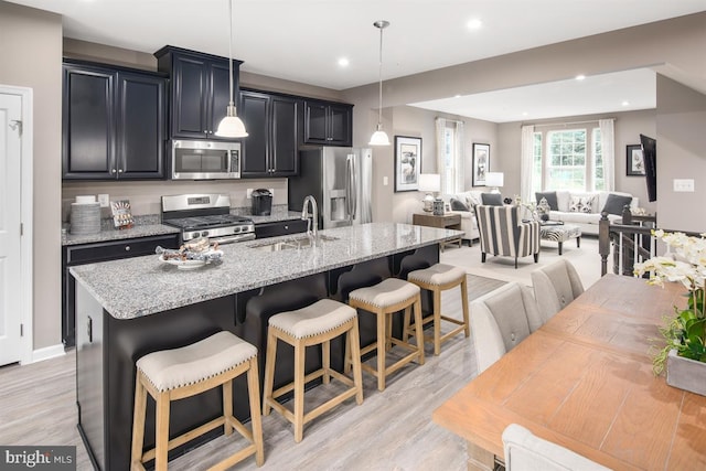 kitchen with a breakfast bar, hanging light fixtures, a kitchen island with sink, and appliances with stainless steel finishes