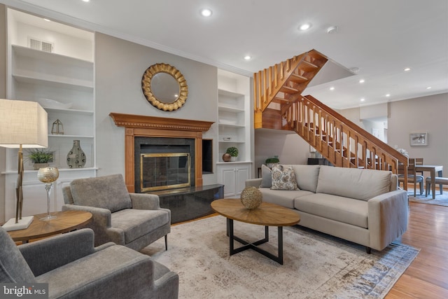 living room with built in features, light hardwood / wood-style flooring, and ornamental molding