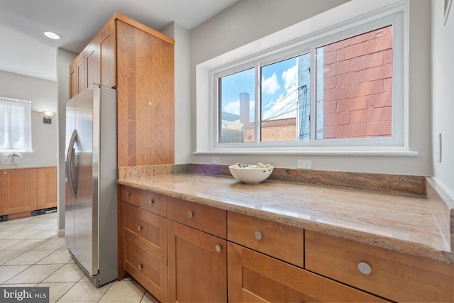 kitchen with light stone countertops, stainless steel fridge with ice dispenser, and light tile patterned floors