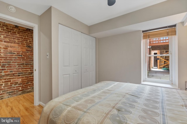 bedroom with hardwood / wood-style flooring, a closet, and brick wall