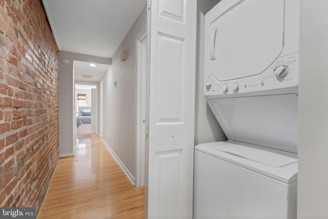 laundry area featuring brick wall, stacked washer and clothes dryer, and light wood-type flooring