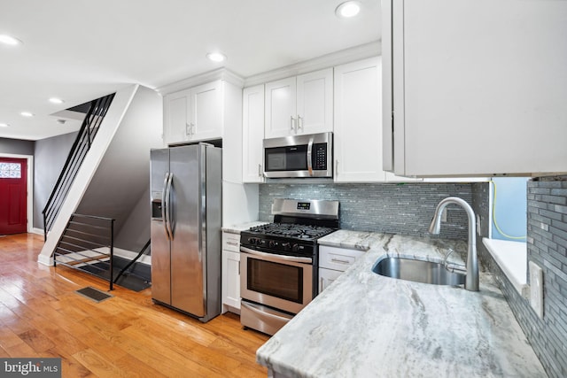 kitchen with backsplash, sink, light wood-type flooring, white cabinetry, and stainless steel appliances