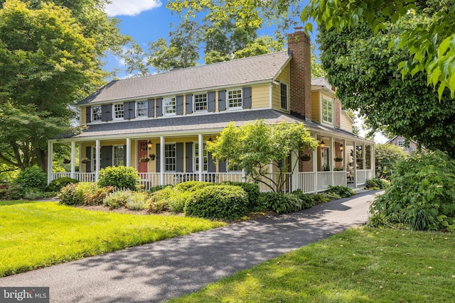 view of front of home with a porch, a chimney, and a front yard