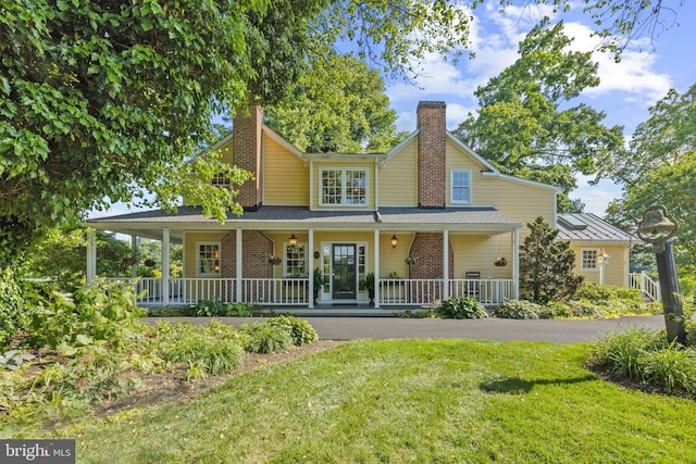 farmhouse inspired home featuring a front lawn, brick siding, covered porch, and a chimney