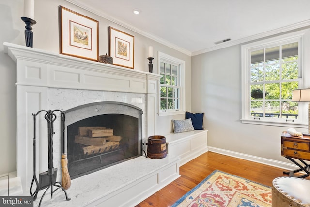 living area featuring wood finished floors, baseboards, visible vents, a high end fireplace, and ornamental molding