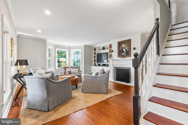 living area with built in shelves, a fireplace with flush hearth, stairs, ornamental molding, and hardwood / wood-style flooring