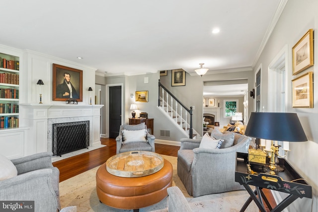 living room featuring a high end fireplace, visible vents, crown molding, stairs, and wood finished floors