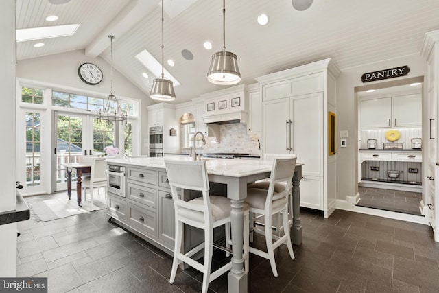 kitchen featuring beam ceiling, high vaulted ceiling, tasteful backsplash, stainless steel appliances, and a skylight