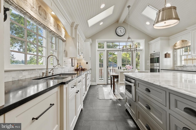 kitchen with beam ceiling, a skylight, gray cabinets, a sink, and tasteful backsplash