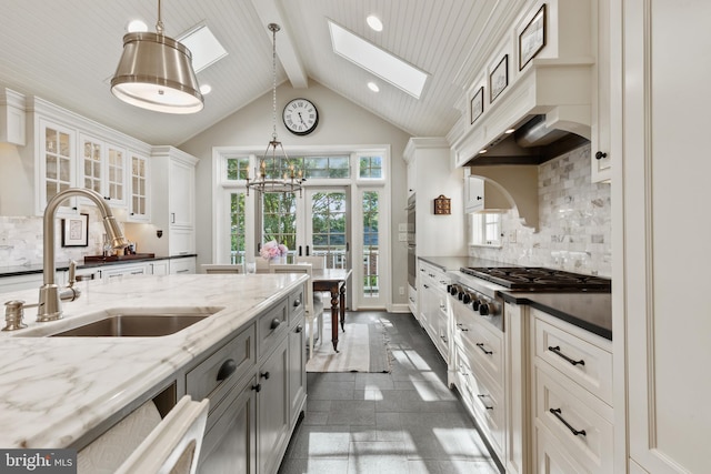 kitchen with a skylight, a sink, stainless steel gas stovetop, glass insert cabinets, and beamed ceiling