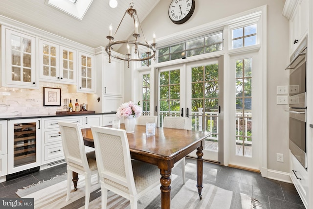 dining space featuring beverage cooler, baseboards, high vaulted ceiling, an inviting chandelier, and french doors