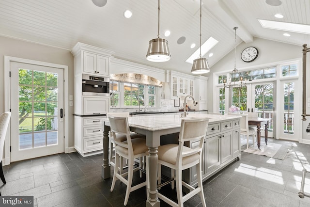 kitchen with beamed ceiling, stone tile floors, decorative backsplash, a skylight, and white cabinets