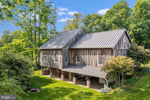 rear view of house featuring a fire pit, a patio, metal roof, a yard, and a standing seam roof